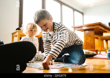 Junge mit Behinderung lösen Puzzle sitzen von Vater und Schwester im Wohnzimmer zu Hause Stockfoto