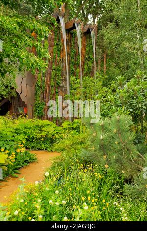 Ein Wasserfall über einer kunststoffgestreifte Felswand, umgeben von Grün, im Medite Smartply Building The Future Garden, entworfen von Sarah Eberle Stockfoto