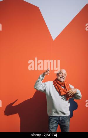 Porträt eines glücklichen älteren Mannes, der gegen eine orangefarbene Wand tanzt Stockfoto