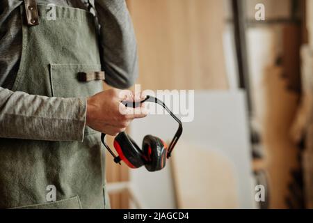 Nahaufnahme eines Mitarbeiters mit geräuschreduzierenden Kopfhörern in Werkstatt, Produktion und Sicherheit, Kopierbereich Stockfoto