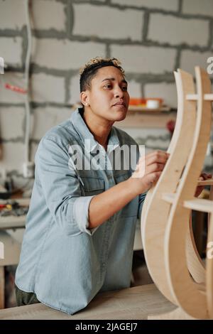Vertikales Porträt einer modernen Tischlerin, die Holzmöbel im Innenraum der Werkstatt entwirft Stockfoto