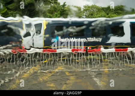 Ein Zug aus Südwest, der die Vine Road von Network Rail passiert und bei starkem Regen Barrieren überquert, Barnes, Südwestlondon, England, Großbritannien Stockfoto