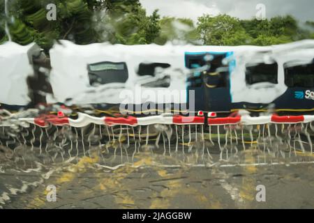 Ein Zug aus Südwest, der die Vine Road von Network Rail passiert und bei starkem Regen Barrieren überquert, Barnes, Südwestlondon, England, Großbritannien Stockfoto
