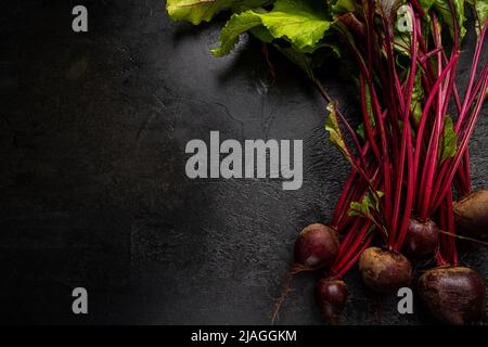 Frische rote Rote Beete mit kraut grünen Blättern auf schwarzem Hintergrund, Draufsicht Stockfoto