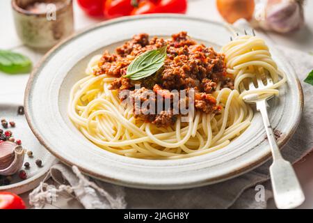 Pasta Spaghetti Bolognese mit Rinderhacksauce, Tomaten, Parmesankäse und frischem Basilikum auf einem Teller auf weißem Fliesenhintergrund. Italienisches Essen Stockfoto