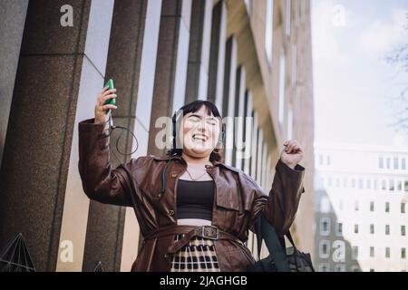 Glückliche junge Frau mit geschlossenen Augen tanzt beim Musikhören über Kopfhörer Stockfoto