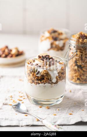 Knuspriges Müsli mit Joghurt, Banane, Nüssen, Schokolade und Honig in einem Glas auf weißem Hintergrund. Gesundes Frühstückskonzept. Stockfoto