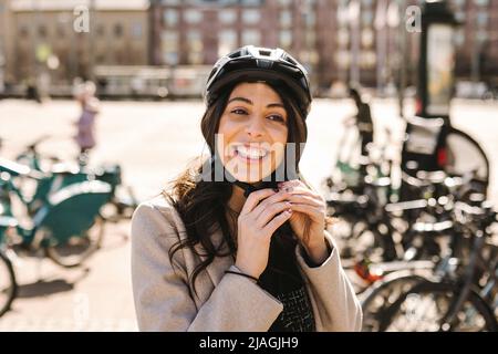 Glückliche Geschäftsfrau mit Helm auf dem Fahrradparkplatz in der Stadt Stockfoto