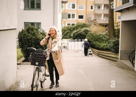 Glückliche Geschäftsfrau, die auf dem Smartphone spricht, während sie mit dem Fahrrad auf dem Fußweg fährt Stockfoto