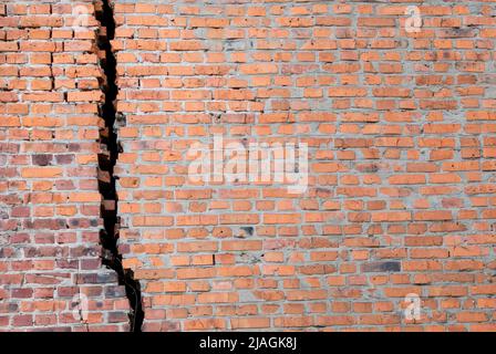 Rote Backsteinmauer mit großem schwarzen Riss Stockfoto