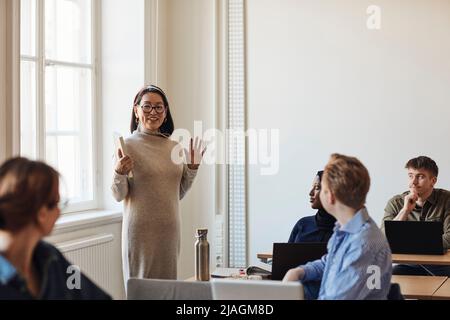 Lächelnde Lehrerin gestikulierte, während sie die Schüler im Klassenzimmer unterrichtete Stockfoto