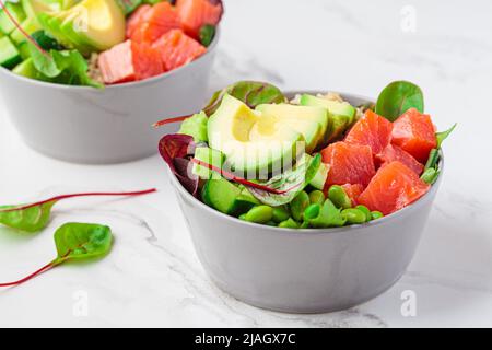 Hawaiian Poke - brauner Reis, Lachs, Edamame, Gurke und Avocado in einer grauen Schüssel, Marmorhintergrund. Fisch frischer Salat für eine gesunde Ernährung. Stockfoto