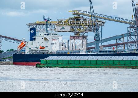 WESTWEGO, LA, USA - 23. MAI 2022: Cargill Getreideaufzug, angedocktes Frachtschiff und vorbeifahrende Barge auf dem Mississippi River in der Nähe von New Orleans Stockfoto