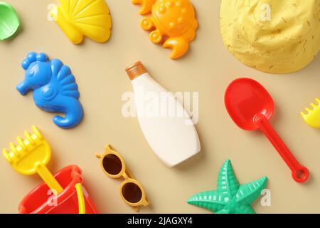 Flache Lay-Komposition mit Sonnencreme-Lotion-Flasche, Baby-Sonnenbrille, Sandformen, panama-Hut auf beigem Hintergrund. Sonnenschutz für Kinder Konzept. Stockfoto