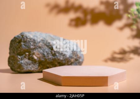 Kreatives Betonstein- und beigefarbenes Podium für Kosmetika oder Produkte mit Schattierungen von grünen Ästen auf beigem Hintergrund. Vorderansicht Stockfoto