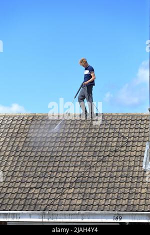 Person, die in der Höhe des Strahls arbeitet und ein Dach ohne Sicherheitsausrüstung oder PSA wäscht. Stockfoto