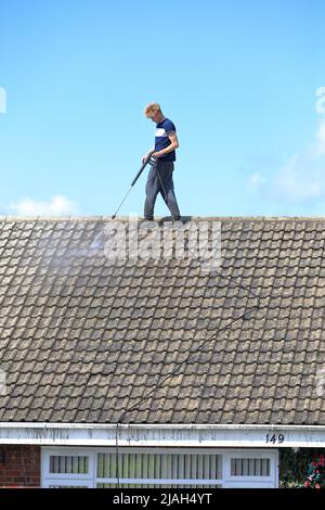 Person, die in der Höhe des Strahls arbeitet und ein Dach ohne Sicherheitsausrüstung oder PSA wäscht. Stockfoto