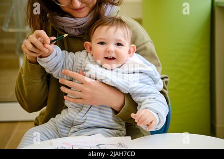 Eine Mutter mit einem Kleinkind-Baby zieht, während sie während eines Besuchs in einer Kinderklinik auf einen Arzt wartet. Ein Jahr altes Kind Stockfoto