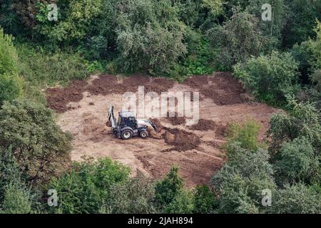 Der Bagger bereitet den Boden auf dem Feld im Wald unter den Bäumen für die Landschaftsgestaltung und Landwirtschaft, Draufsicht Stockfoto