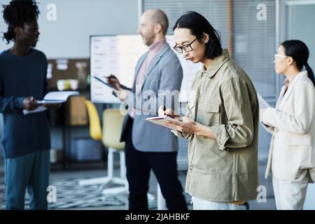 Seitenansicht Porträt eines jungen asiatischen Mannes, der während eines Bildungsseminars im Büro mit einer Gruppe von Menschen Nippes auf die Zwischenablage nimmt, Kopierraum Stockfoto