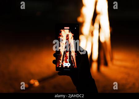 Ein Lagerfeuer mit Funken bei Dunkelheit. Orangefarbene Flamme im Freien. Aufnahmen mit dem Mobiltelefon Stockfoto