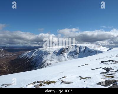 Blick auf den verschneiten und schneebedeckten Munro, Beinn Bhrotain und den Glen Geusachan, mit Glen Dee und den Forest of Mar in der Ferne. Stockfoto