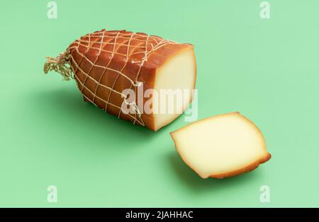 Nahaufnahme mit einem großen Stück geräuchertem Käse auf einem grünen Tisch. Geräucherter Käsefaden, mit einem Stück in Scheiben gewickelt, minimalistisch auf grünem Hintergrund Stockfoto