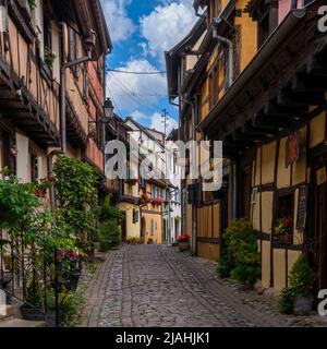 Eguisheim, Frankreich - 29. Mai 2022: Enge gepflasterte Straße mit bunten historischen Fachwerkhäusern Stockfoto