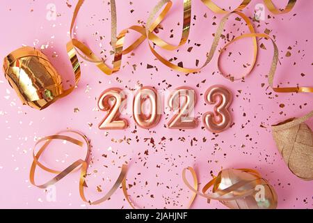 Draufsicht auf Roségold Zahlen 2023 mit Goldkonfetti und Glitzer auf rosa Hintergrund.Festliches Banner, flach Lay-Stil. Stockfoto