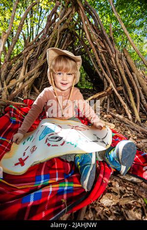 Junge im Hut mit Schatzsuche Karte über Hütte von Zweigen Stockfoto