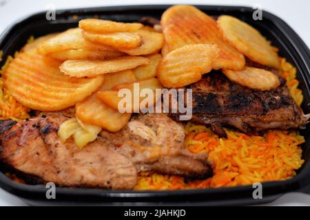 Arabisch-syrische Küche von Holzkohle gegrilltes Huhn mit buntem Basmati-Reis und gebratenen Chips Kartoffeln in einem schwarzen Einwegteller usu serviert Stockfoto