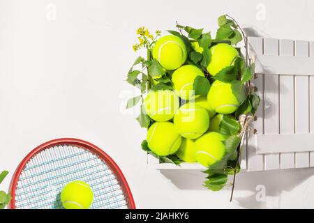 Tennisbälle in einer Holzkiste und Schläger auf weißem Hintergrund Stockfoto