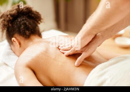 Nahaufnahme der männlichen Hände, die sich von einer jungen afroamerikanischen Frau im SPA massieren lassen Stockfoto