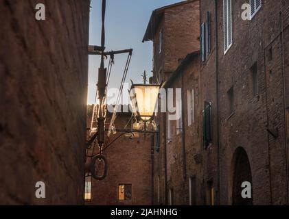 Veraltete Straßenlaternen, die von Staub, Schmutz und Spinnennetz bedeckt sind, an einer Gebäudewand montiert und von der Sonne des Sonnenuntergangs beleuchtet sind Stockfoto