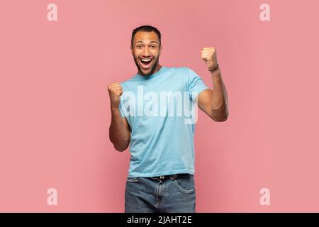 Überglücklich schreiender junger schwarzer Mann, der MIT beiden Händen auf pinkem Studiohintergrund Ja gestikulierte Stockfoto