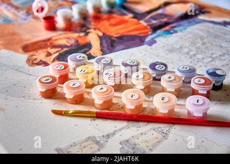 Halb gemalte Malerei nach Zahlen mit Acrylfarbe Gläser und ein Pinsel. Selektiver Fokus, Lichtunschärfe, Unschärfe. Stockfoto