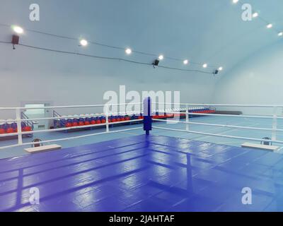 Eine Sporthalle mit leeren Zuschauersitzen und einem Kampfring wird von hellen Scheinwerfern beleuchtet. Foto vom Telefon Stockfoto