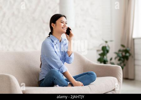 Fröhliche chinesische Frau, die zu Hause am Handy spricht Stockfoto