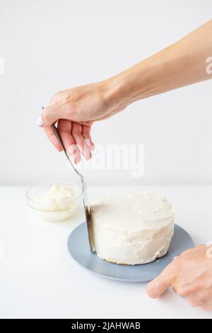 Köstliche cremige Torte, die das Mädchen mit einem Spatel über die Schlagsahne verteilt, ist der Kuchen bereit zur Dekoration Stockfoto