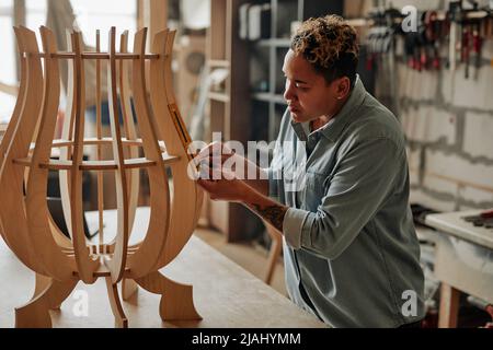 Seitenansicht Porträt einer modernen Tischlerin, die Holzmöbel im Innenraum der Werkstatt entwirft Stockfoto