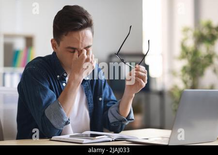 Mitarbeiter Im Millenial Office, Der Nach Der Arbeit Mit Dem Laptop Am Schreibtisch Die Augen Reibt, Müde Stockfoto