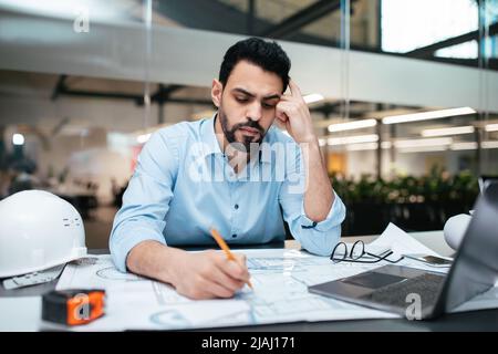 Traurig ernst nachdenklich attraktive tausendjährige arabische Mann Ingenieur mit Bart arbeitet mit Projektzeichnungen Stockfoto