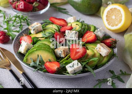 Gesunder Salat mit Erdbeeren, Avocado, Rucola und Käse dor blau, mit Balsamico auf hellgrauem Hintergrund gekleidet Stockfoto