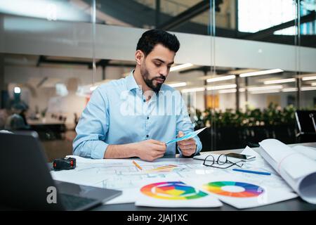 Beschäftigt ernst attraktiven tausendjährigen arabischen Kerl Designer mit Bart arbeitet mit Farbpaletten am Arbeitsplatz Stockfoto