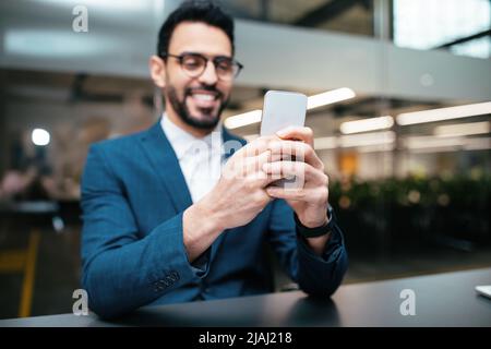 Happy Handsome tausendjährigen islamischen Geschäftsmann mit Bart in der Brille tippt auf dem Smartphone im Büro Stockfoto