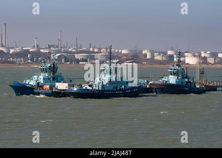 Fawley, Southampton, England, Großbritannien. 2022. Drei Ozeanschlepper neben einem Steg mit Hintergrund der Fawley Raffinerie, Kaminen und Rauchschornsteinen, Stockfoto