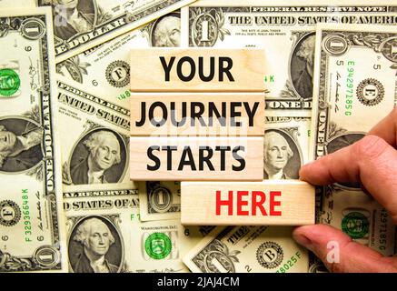 Ihre Reise beginnt hier Symbol. Konzeptwörter Ihre Reise beginnt hier auf Holzblöcken auf einem wunderschönen Hintergrund aus Dollarscheinen. Business, motiva Stockfoto