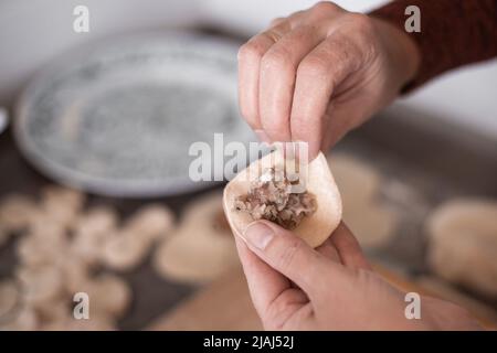 Eine Frau in der Küche formt Knödel aus Teig mit Fleischfüllung. Kochen köstliche hausgemachte Knödel. Stockfoto