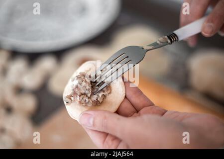 Eine Frau in der Küche formt Knödel aus Teig mit Fleischfüllung. Kochen köstliche hausgemachte Knödel. Stockfoto