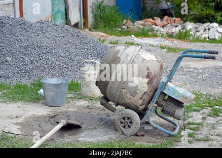 Betonmischer mit Sand und Steinen auf dem Hof. Alte rostige mobile Betonmischer auf der Straße. Tragbarer tragbarer Betonmischer. Stockfoto